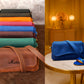 Colorful handbags stacked and a blue handbag with matching sandal on a table.