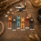 Six leather keychain wallet charms in different colors (Tawny, Gray, Denim, Yellow, Brown, Chocolate) arranged on a rustic wooden table with decorative props like keys, coins, rope, and fairy lights.