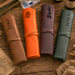 Four personalized leather roll-up wallets or organizer sleeves in brown, orange, burgundy, and sage green, each embossed with a name (Jake, Aiden, Sophia, JOEY) and styled on a rustic wooden tabletop.