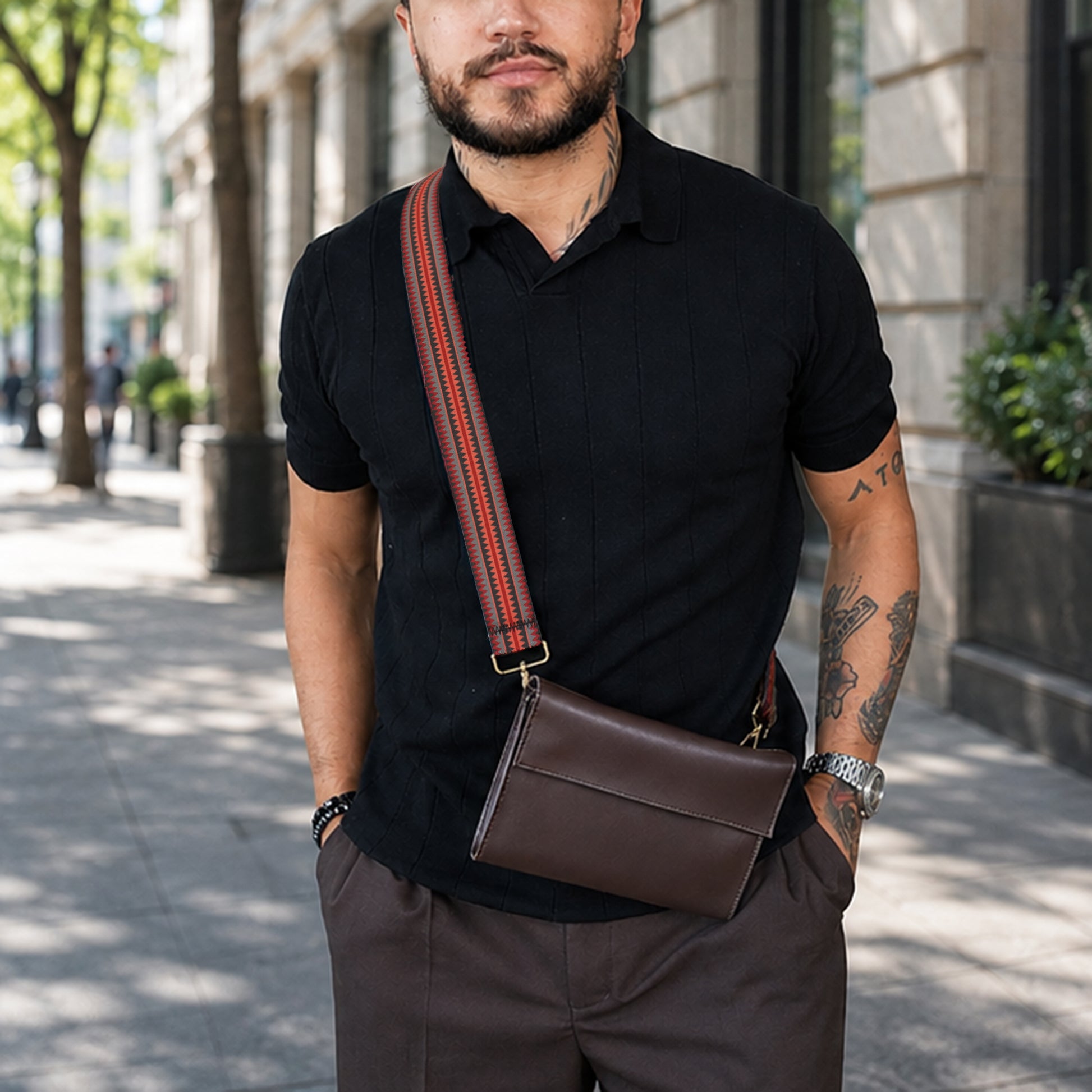 Man wearing a black shirt and brown pants with a brown leather bag on a city street.
