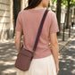 Woman wearing a pink shirt and carrying a matching pink crossbody bag with a decorative strap on a sunny street.