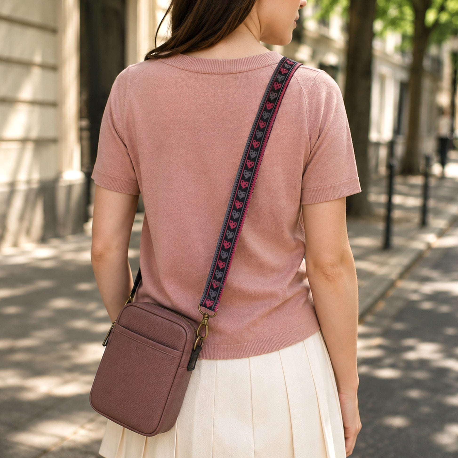 Woman wearing a pink shirt and carrying a matching pink crossbody bag with a decorative strap on a sunny street.