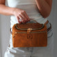 Person holding a brown leather handbag with a visible brand logo.