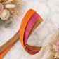 Three colorful belts (orange, pink, brown) on a marble surface with decorative flowers.