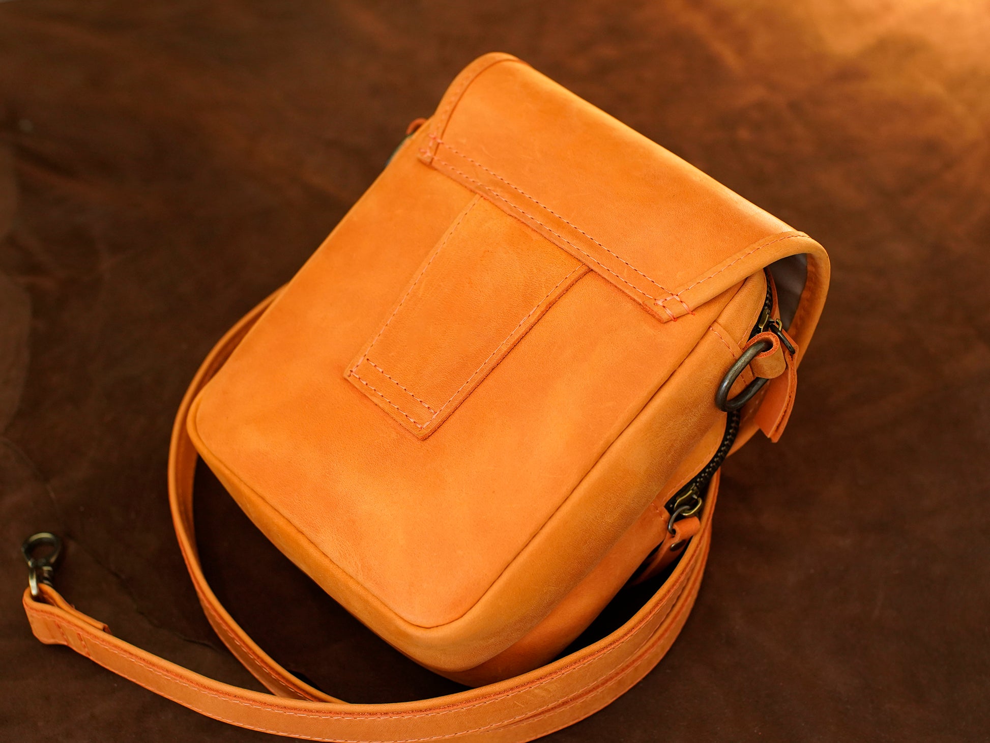 Orange leather crossbody bag on a brown background