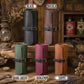 Six rolled leather cylindrical cases or sleeves in different colors are arranged on a rustic wooden surface with vintage props. The top row shows two dark leather rolls labeled BLACK and CHOCOLATE, and the bottom row shows four suede-like leather rolls labeled DARK GREEN, BURGUNDY, and TAWNY.