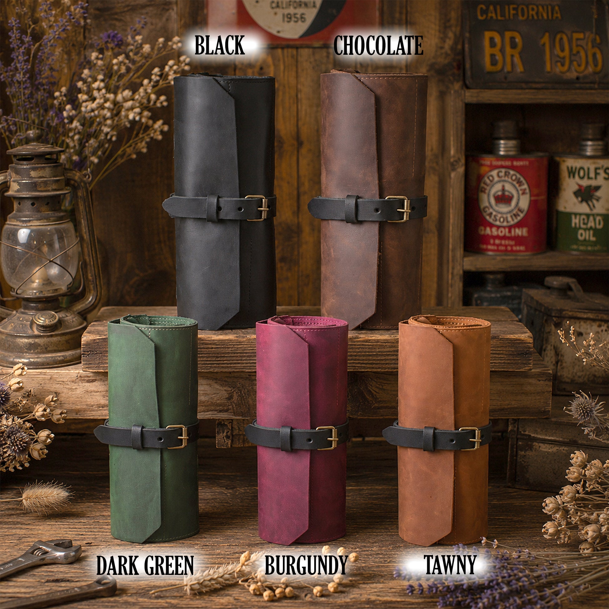 Six rolled leather cylindrical cases or sleeves in different colors are arranged on a rustic wooden surface with vintage props. The top row shows two dark leather rolls labeled BLACK and CHOCOLATE, and the bottom row shows four suede-like leather rolls labeled DARK GREEN, BURGUNDY, and TAWNY.