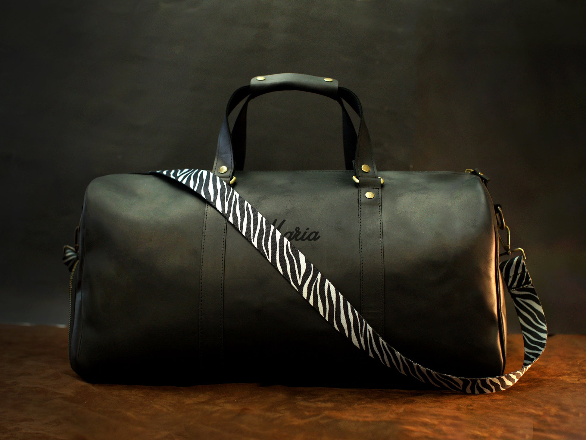 Green leather duffel bag with zebra pattern strap on a wooden surface