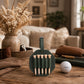 A dark green leather golf club addresser set with wooden tees, displayed on a rustic wooden table next to a golf ball, with a cozy living room background.