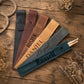 Five personalized leather drumstick pouches in different colors are arranged in a fan shape on a rustic wooden table, with dried flowers and a jar of beads as props. The pouches are custom monogrammed or printed with names: M, SJ, FOSTER, DANIEL, Abigail, and Russell.