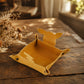A mustard yellow felt dog toy tray with a dog silhouette on the back, displayed on a rustic wooden table with dried flowers in the background.