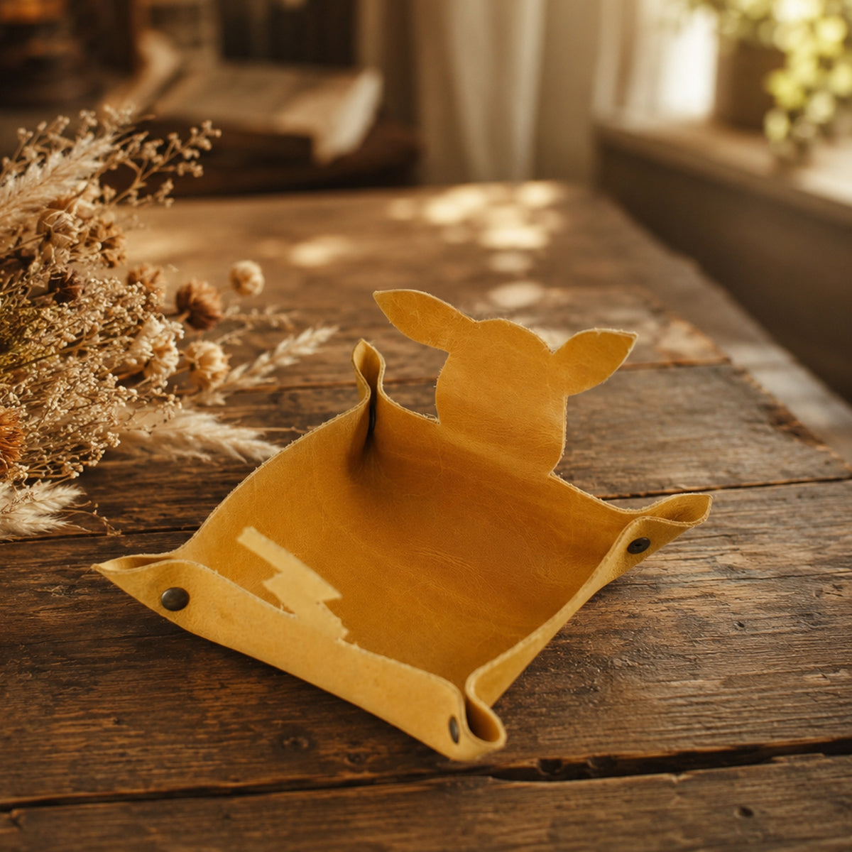 A mustard yellow felt dog toy tray with a dog silhouette on the back, displayed on a rustic wooden table with dried flowers in the background.