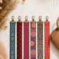 Set of six patterned lanyards on a light surface with a brown handbag and dried flowers.