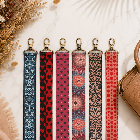 Set of six patterned lanyards on a light surface with a brown handbag and dried flowers.