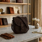 Brown leather bag on a marble surface with shelves and decor in the background