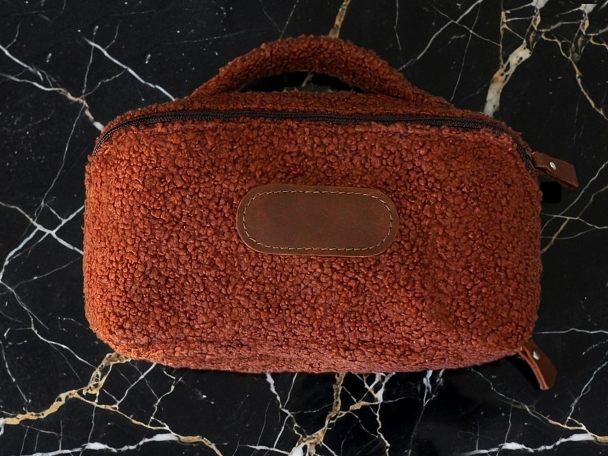 Brown textured bag with leather patch on a black marble surface