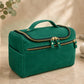 Green toiletry bag with gold zippers on a beige surface with decorative items.