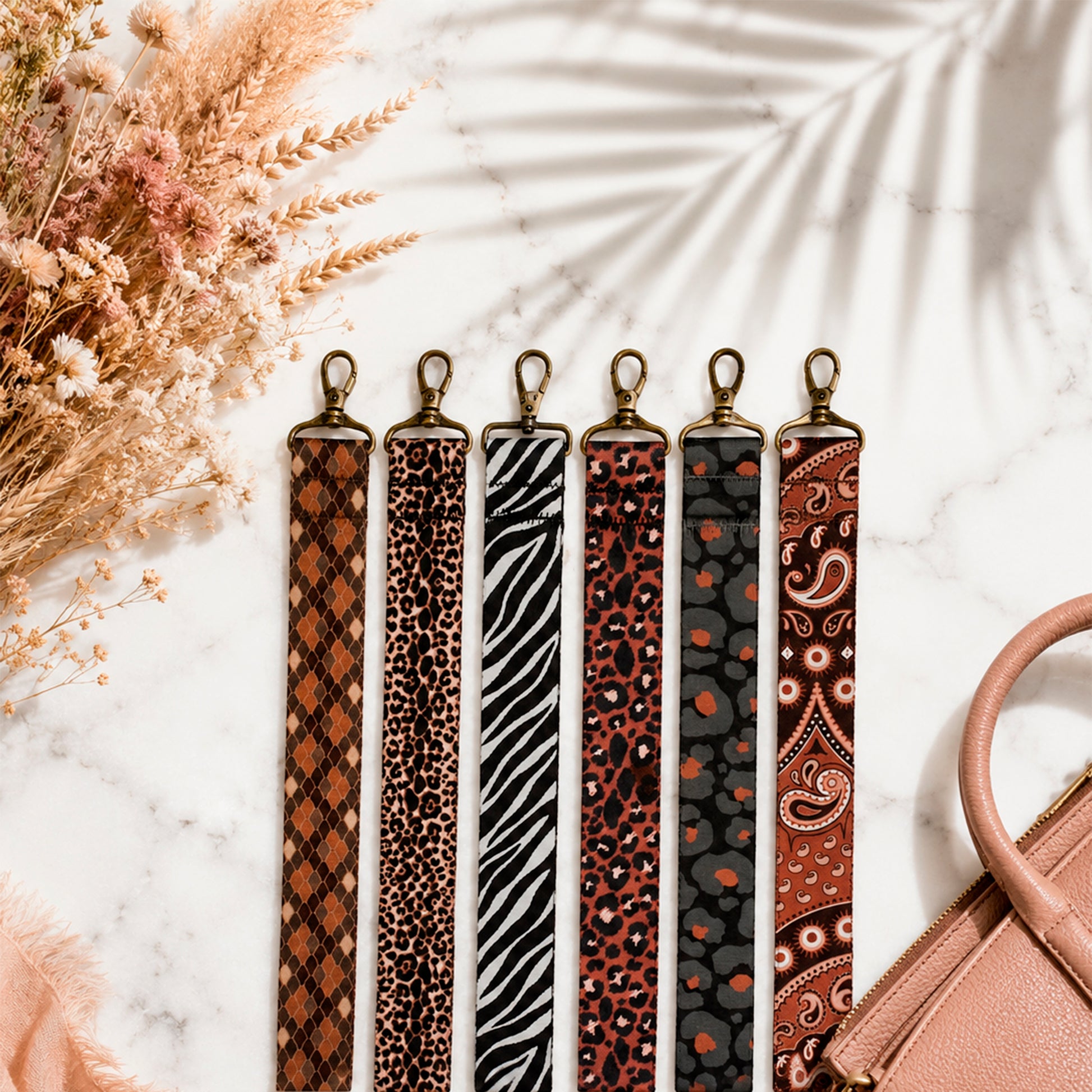 Set of patterned straps on a marble surface with dried flowers and a handbag.