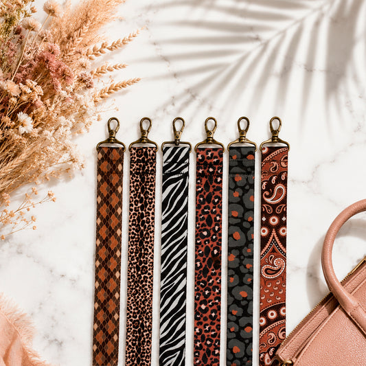 Set of patterned straps on a marble surface with dried flowers and a handbag.