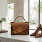 Brown leather handbag and high-heeled shoes on a marble surface with a neutral background