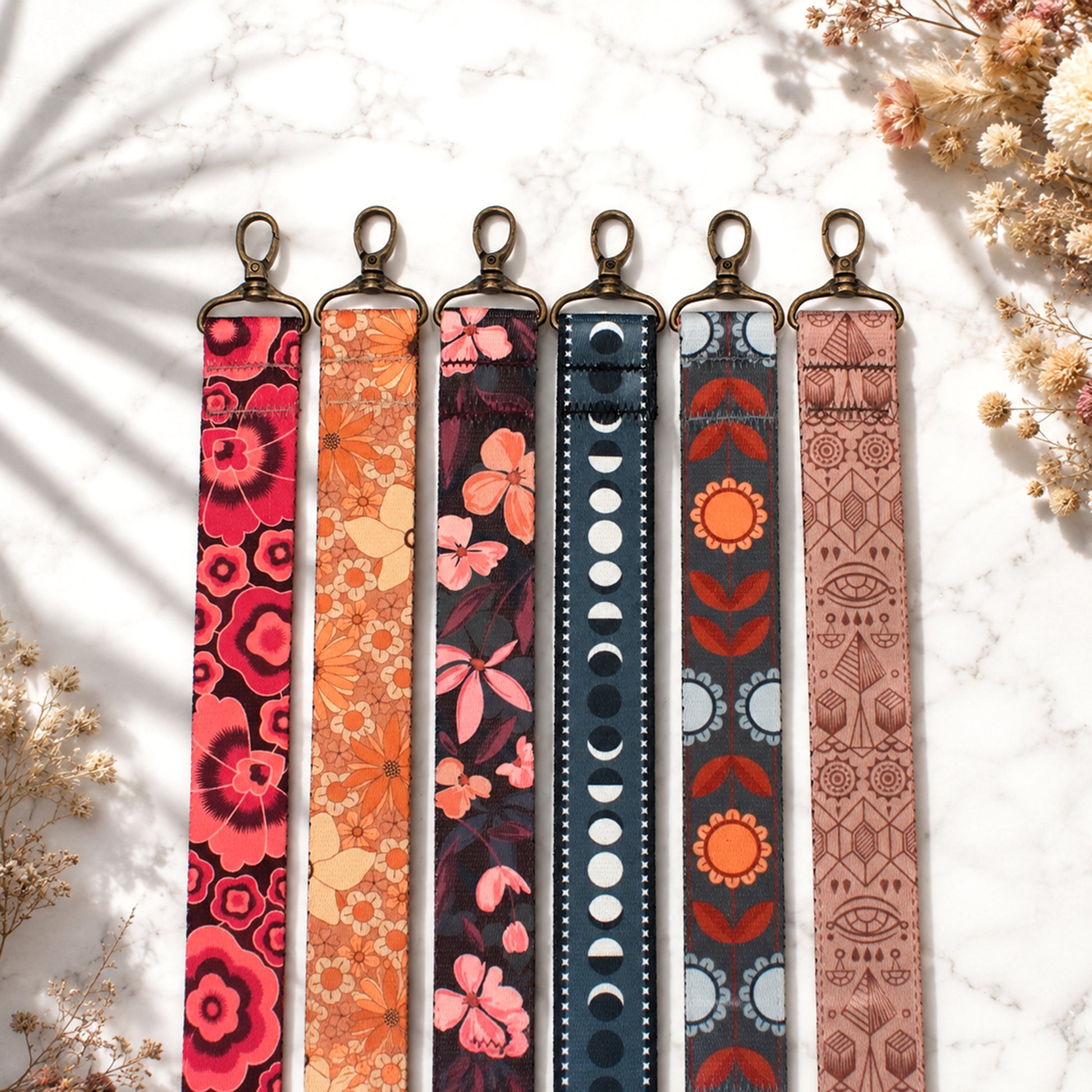 Set of six patterned lanyards on a light background with dried flowers.