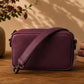 Burgundy crossbody bag on a wooden surface with a vase and books in the background