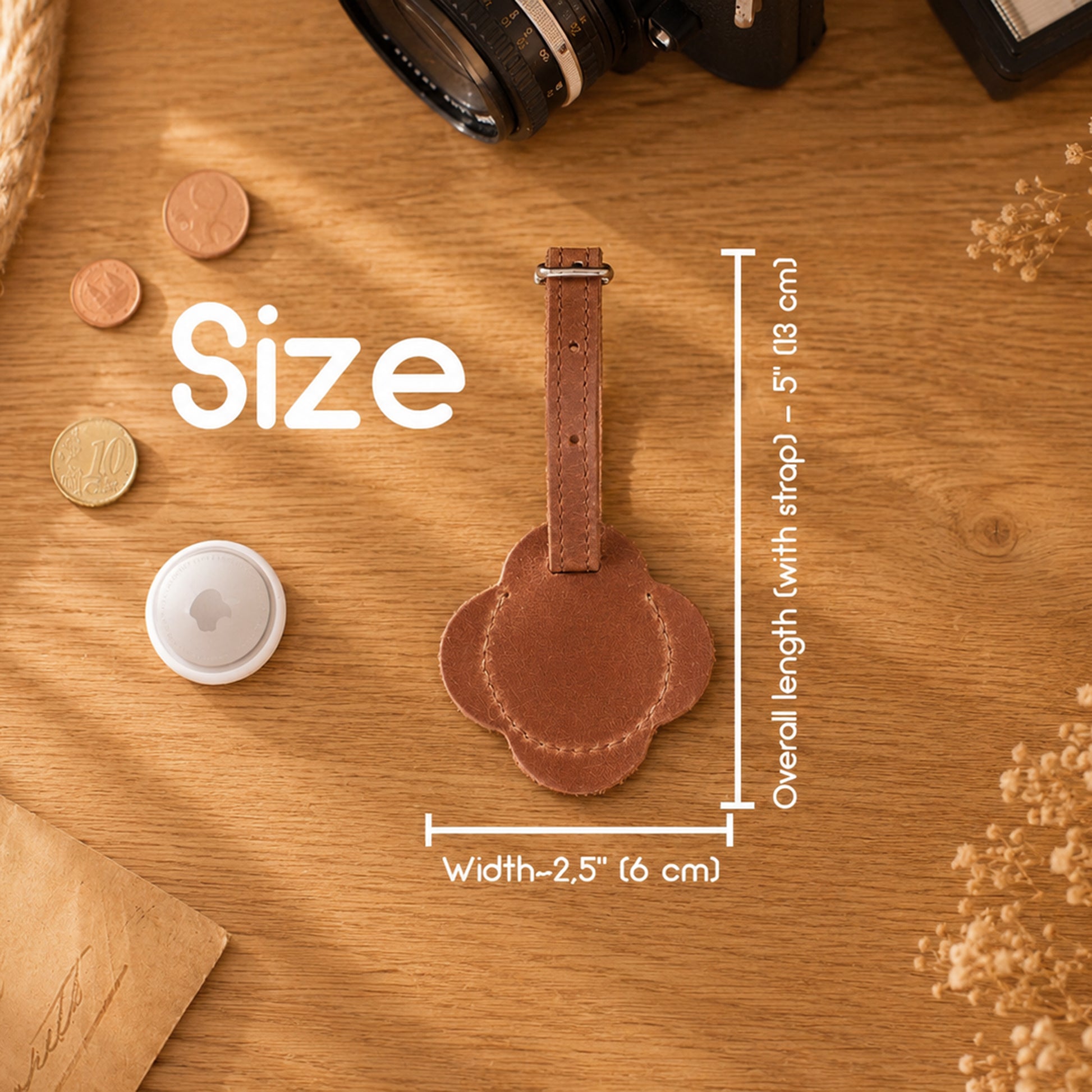 A brown leather luggage tag with a strap is shown on a wooden tabletop with overlaid size measurements reading 2.5 inches wide by overall length with strap around 5 inches.