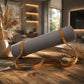 A gray textured yoga mat with tan straps and a matching tan carrying strap, resting on a rustic wooden table in a warm, modern interior setting.