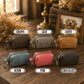 Six small zip pouches with keychains are arranged on a wooden table, each labeled with a color name: Brown, Gray, Tawny, Denim, Pink, and Chocolate. The pouches come in different colors and are shown in a styled indoor setting with dried flowers, books, and a framed dog portrait in the background.