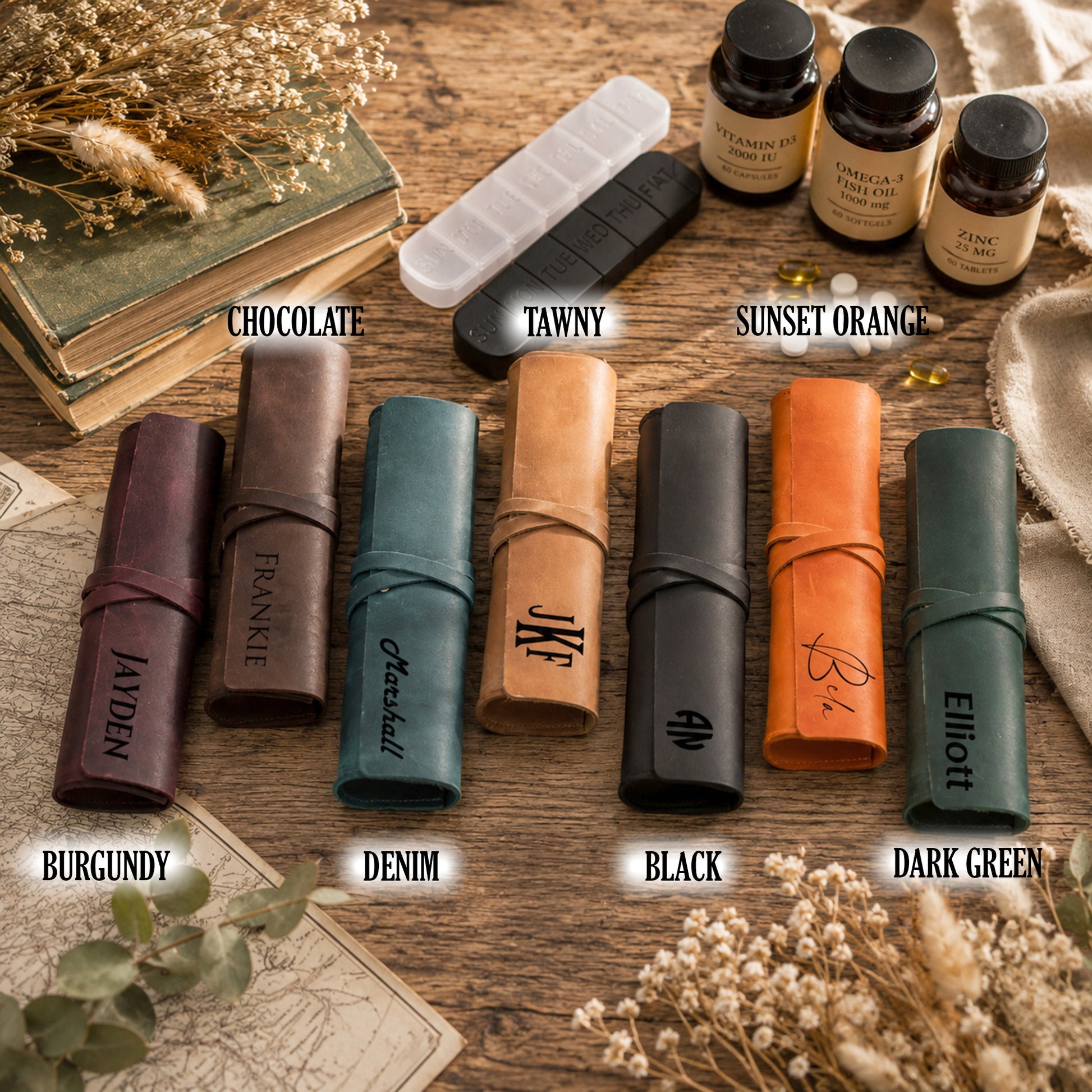 Eight leather travel-sized lip balm cases in assorted colors are arranged on a rustic wooden surface with decorative books, dried flowers, and small supplement bottles. The cases are labeled with names and colors: Burgundy, Denim, Black, Dark Green, Chocolate, Tawny, and Sunset Orange.