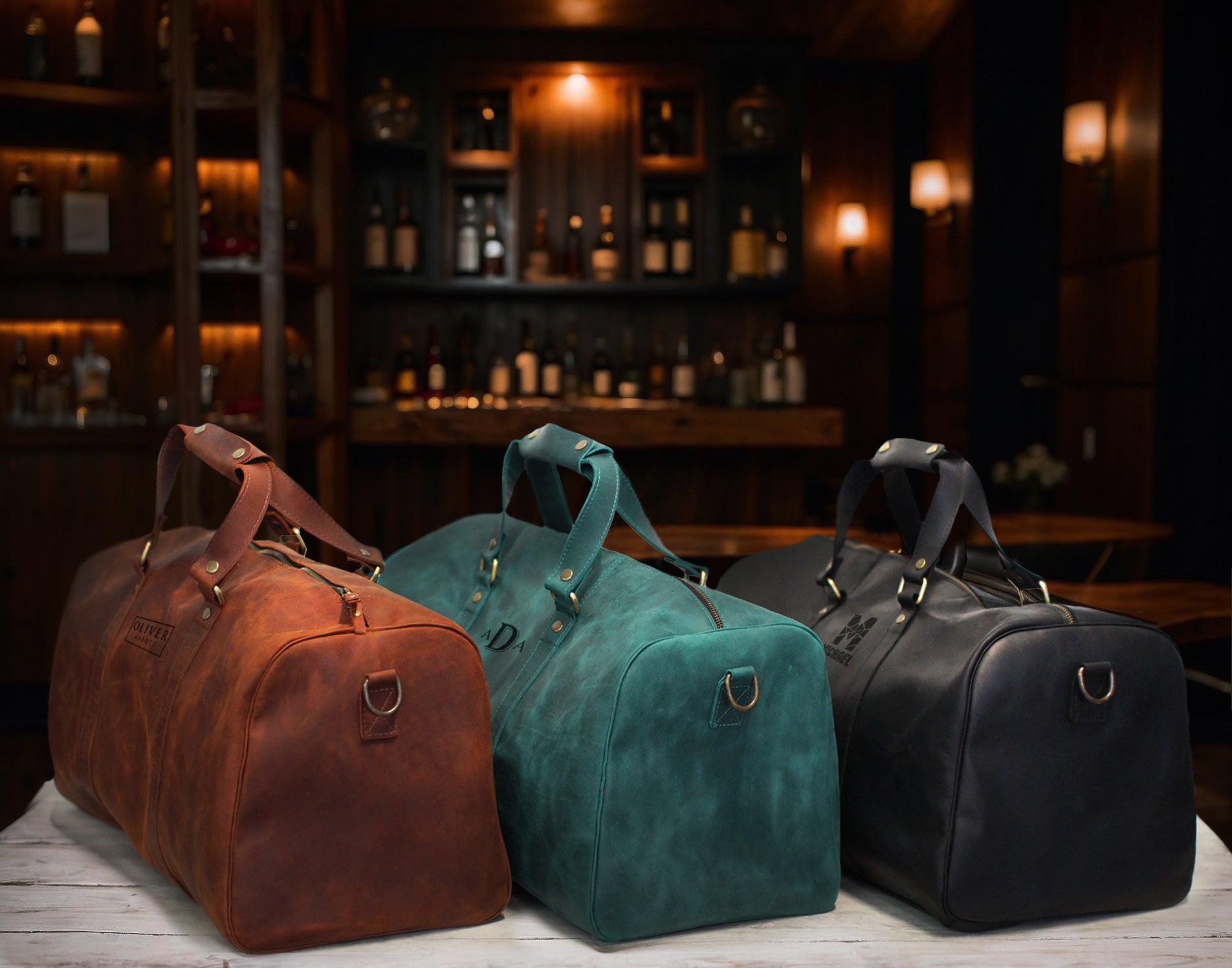 Three leather duffel bags in brown, green, and black on a wooden surface with a bar background.