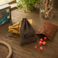 Three personalized leather drawstring pouches in brown, tan, and dark brown are arranged on a rustic wooden table with red polyhedral gaming dice scattered outside one pouch. The center pouch is personalized with the name 'Kevin' in black script.
