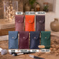Six small leather pouches or cases shown in different colors on a styled tabletop: Tawny, Sunset Orange, Chocolate, Denim, Burgundy, and Black, with labels above and below. The products are arranged with makeup brushes, books, and decorative vases in the background.