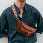 Person wearing a brown leather waist bag with decorative strap against a white background