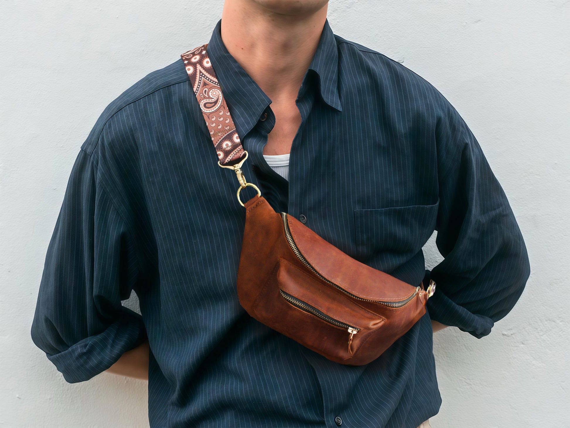 Person wearing a brown leather waist bag with decorative strap against a white background