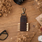 A dark brown leather pencil case with a metal clip, styled on a wooden desk with dried flowers, glasses, and a camera.