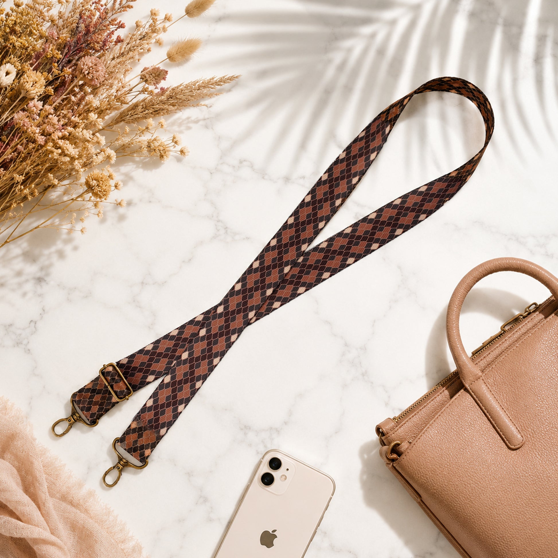 Patterned strap, beige handbag, and smartphone on a light surface with flowers.
