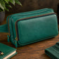 Green leather crossbody bag on a wooden surface with a plant and bottle in the background