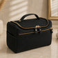Black cosmetic bag with gold zippers on a beige surface