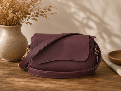 Purple handbag on a wooden surface with a vase of dried flowers in the background
