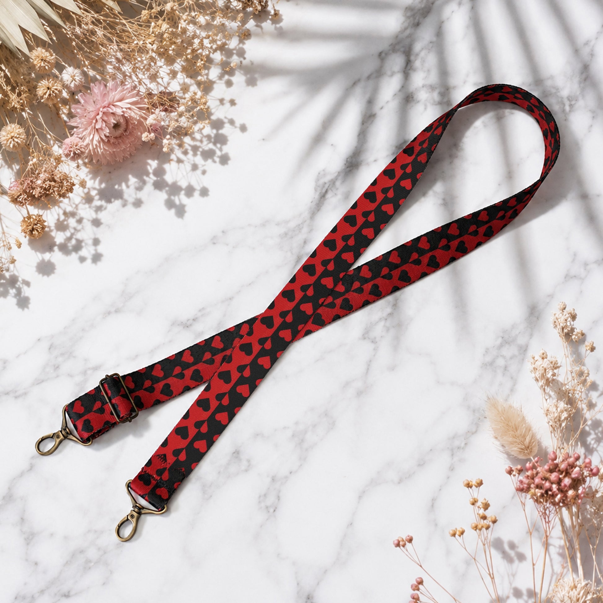 Red and black patterned lanyard on a marble surface with dried flowers.