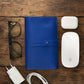 Blue leather  cable organizer, glasses, white Apple products on a wooden surface