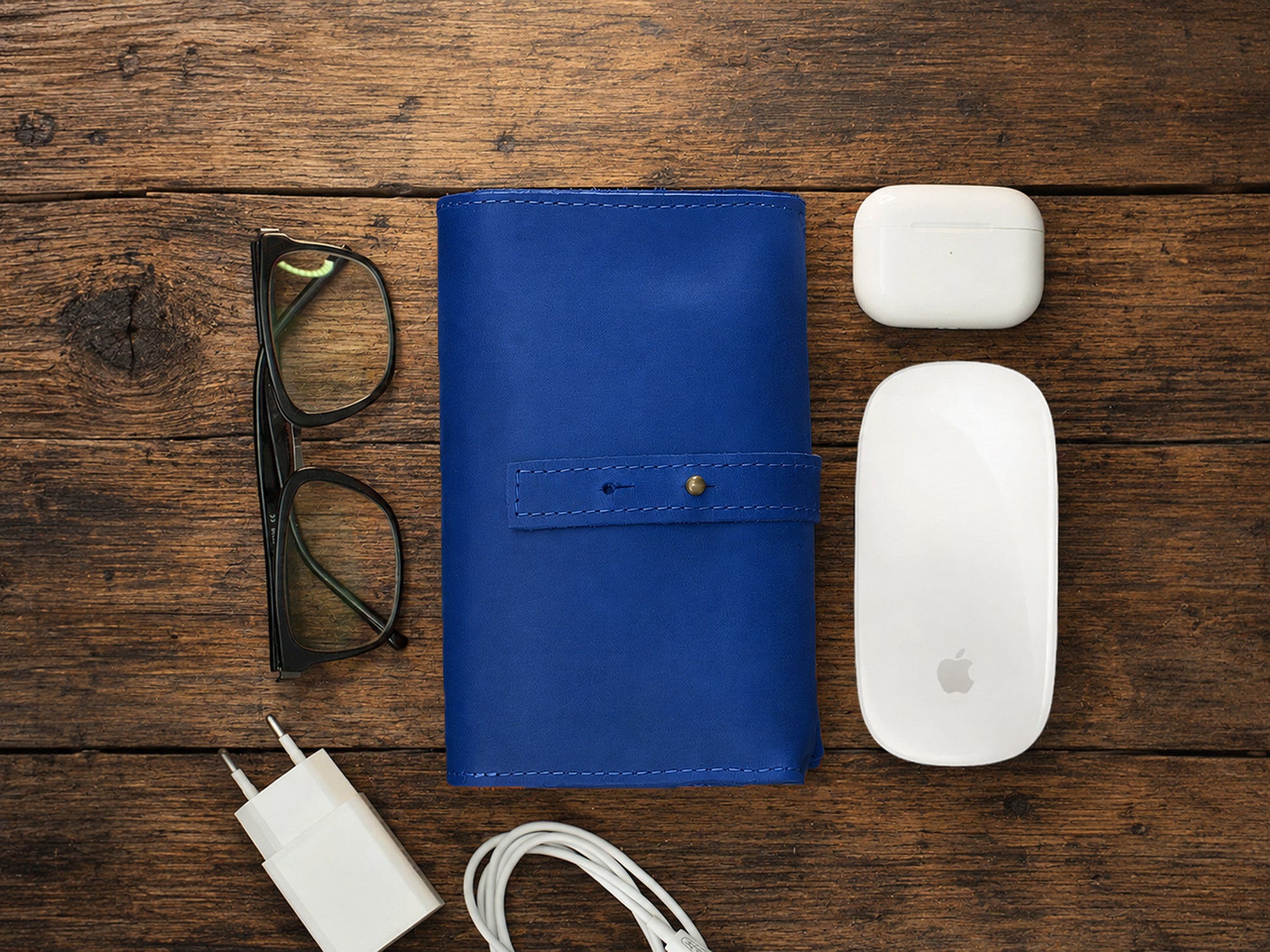 Blue leather  cable organizer, glasses, white Apple products on a wooden surface