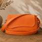 Orange handbag on a wooden surface with a vase and plant in the background