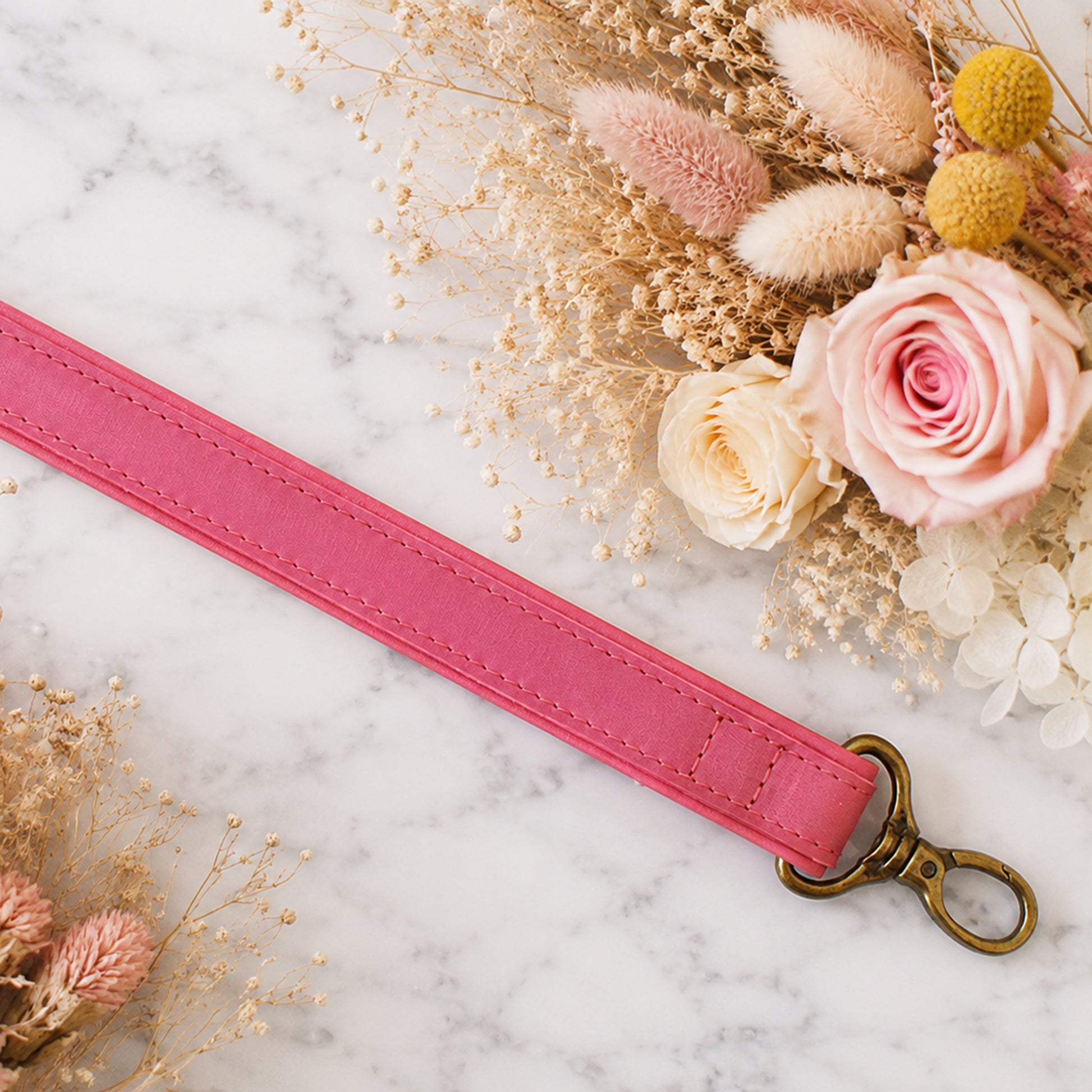 Pink leather strap with a gold clasp on a marble surface with flowers.