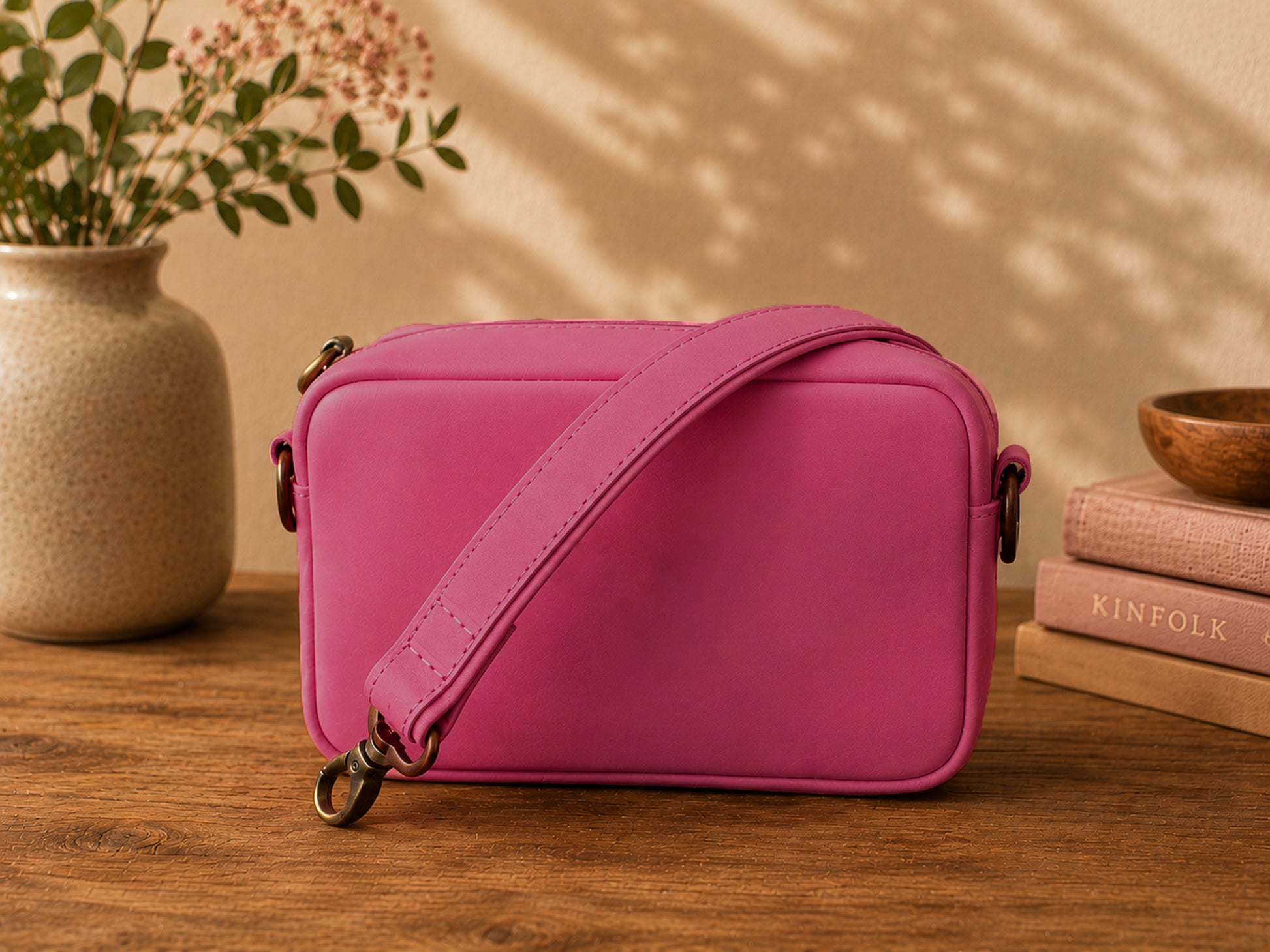 Pink crossbody bag on a wooden surface with a vase and books in the background