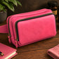 Pink leather crossbody bag on a wooden surface with a notebook and plant in the background