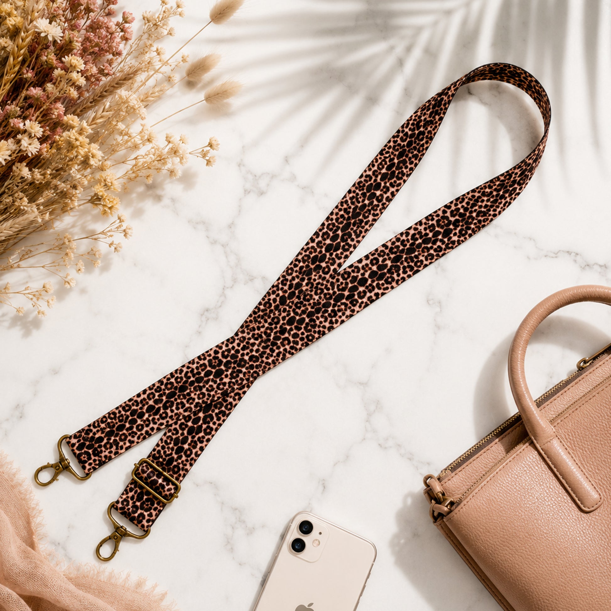Leopard print strap with gold hardware on a marble surface with a phone and handbag.