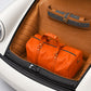 Orange duffel bag in a car trunk with a white background