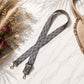 Floral patterned strap with gold hardware on a light surface with dried flowers and a beige bag.